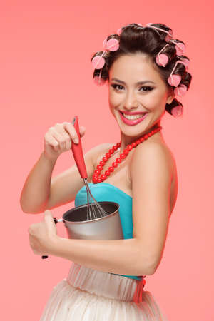 Cooking with pleasure. Happy young housewife whisking something in a panの写真素材