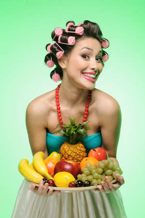 Fruit time. Happy young housewife holding a plate with fruitsの写真素材