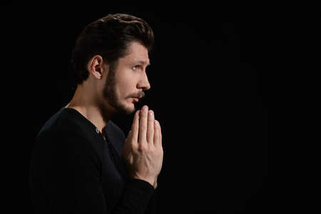 Man praying to God. Side view of bearded man praying and holding his hands claspedの写真素材