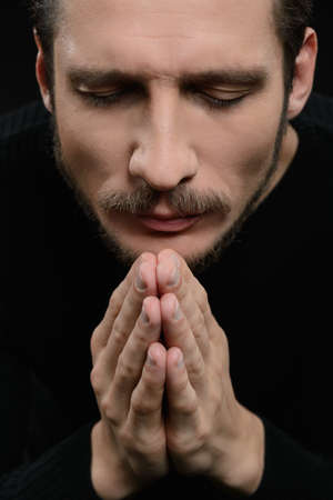 Praying with eyes closed. Devout bearded man praying and holding his hands clasped while isolated on blackの写真素材