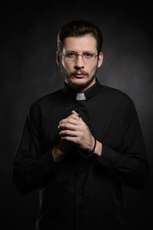 Praying priest. Portrait of priest standing isolated on blackの写真素材