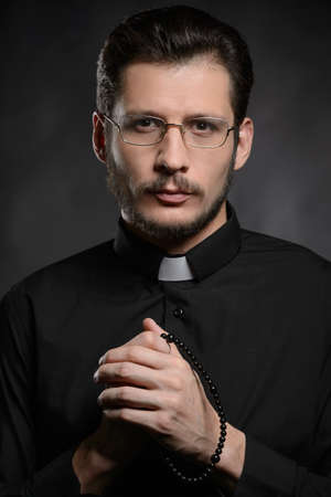 Priest with rosary beads. Portrait of priest standing isolated on blackの写真素材