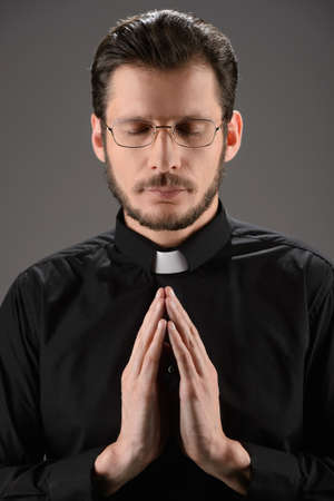 Priest praying to God. Portrait of priest praying while standing isolated on blackの写真素材
