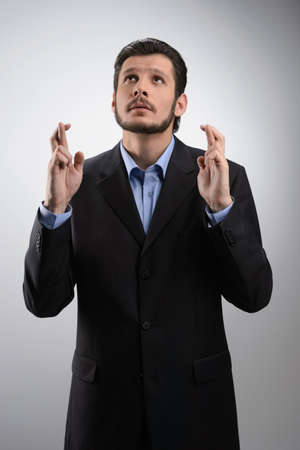 Keeping his fingers crossed. Businessman standing with his fingers crossed against grey backgroundの写真素材