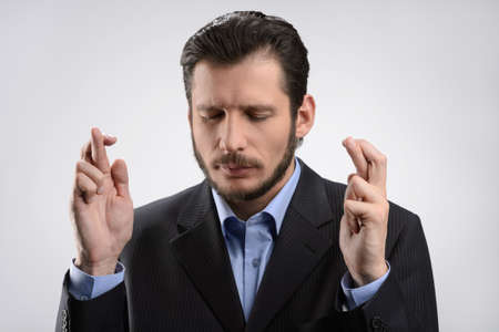 Businessman keeping his fingers crossed. Businessman standing with his fingers crossed against grey backgroundの写真素材
