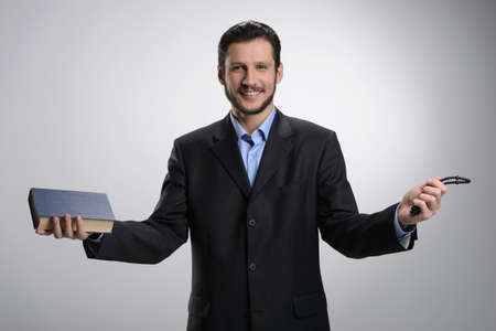Religious businessman. Cheerful bearded man in formalwear holding the Holy Bible and rosary beads in his hands while isolated on greyの写真素材