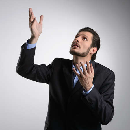 Talking to God. Bearded businessman in formalwear standing with his hands raised up while isolated on greyの写真素材