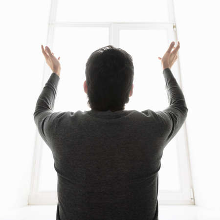The miracle. Rear view of man standing in front of the window with his hands raised upの写真素材