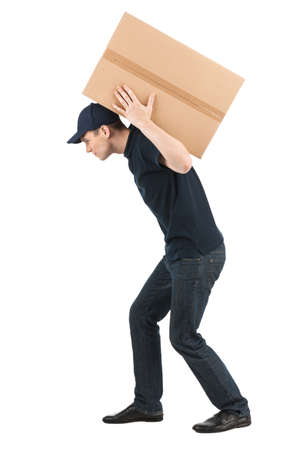 Heavy box. Side view of young deliveryman carrying a big cardboard box while isolated on whiteの写真素材