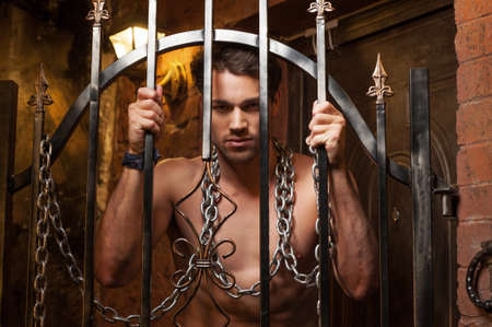 Sexy man standing behind metal gates. With metal chain on neckの写真素材