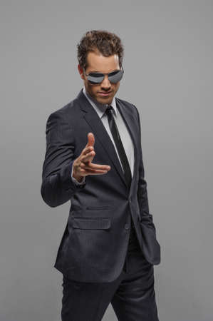 Youï¿½e the next! Confident young businessmen in sunglasses standing isolated on grey and pointing on cameraの写真素材