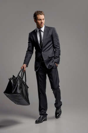 Businessman with suitcase. Full length of confident young businessmen in carrying a suitcase while isolated on greyの写真素材
