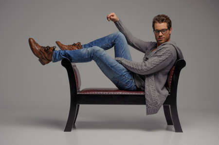 Relaxed young men. Handsome young men in glasses sitting on the chair and looking at camera while isolated on greyの写真素材