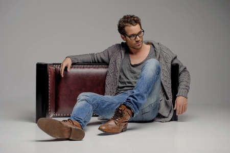 Handsome guy.  Handsome young men in glasses sitting on the floor and looking away while isolated on greyの写真素材