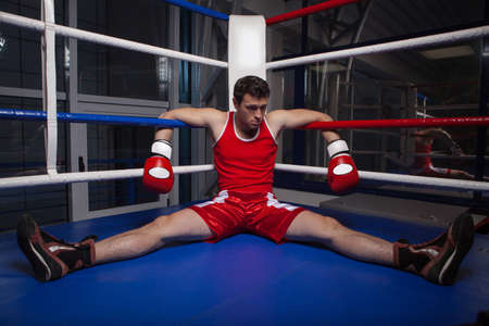 Defeated boxer. Frustrated young boxer sitting on the boxing ringの写真素材