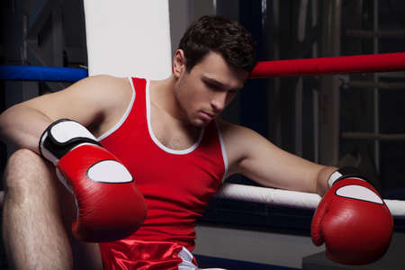 Defeated boxer. Disappointed young boxer sitting on the boxing ring and looking downの写真素材