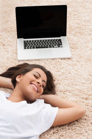 Leisure time. Top view of cheerful young women lying down near her laptop with her head in hands