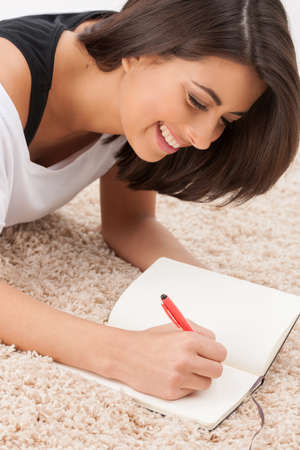 Making notes. Cheerful young women lying down on the floor and making notes at her note padの写真素材