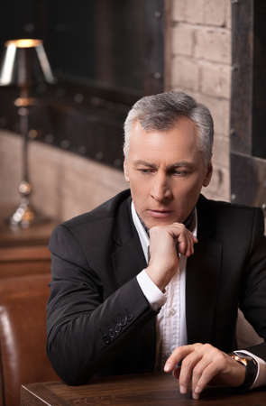 Businessman thinking about options. Thoughtful mature businessman sitting with his hand on chin and looking awayの写真素材
