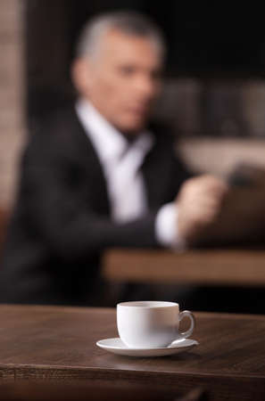 Break time. Mature businessman reading a newspaper with a cup of coffee on the foregroundの写真素材