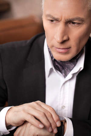 Worried businessman. Worried mature businessman checking the time and looking awayの写真素材