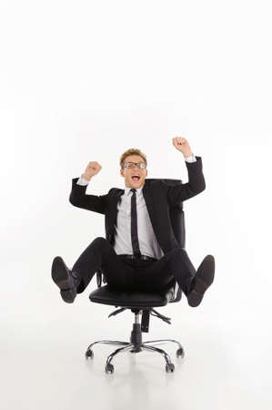 Businessman having fun. Cheerful young businessman sitting on the office chair with his arms raised while isolated on whiteの写真素材