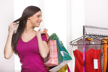 Retail store. Cheerful young woman with shopping bags looking at the dresses in retail storeの写真素材