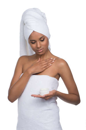 Skin care. Beautiful young women in towel spreading cream over the body while standing isolated on whiteの写真素材