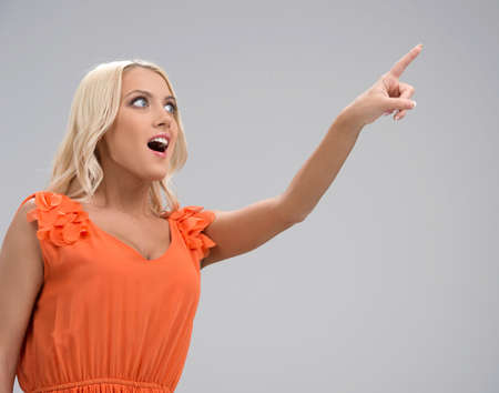 Excited beautiful girl pointing with finger. Isolated on greyの写真素材