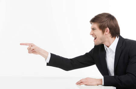 Aggressive businessman. Side view of angry young businessman shouting and pointing away while isolated on whiteの写真素材