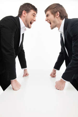 Menï¿½ confrontation  Two angry young business people standing face to face and holding their fists at the table while isolated on whiteの写真素材