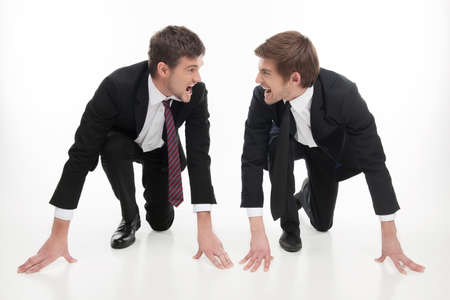 Business competition  Two angry young business people standing at the start line and looking at each other while isolated on whiteの写真素材