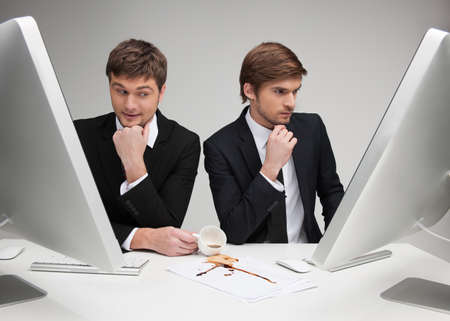 Dirty business  Young man in formalwear pouring coffee on the documents while another man working at the computerの写真素材