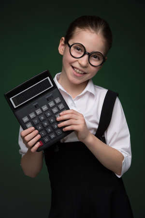Little finance advisor. Happy little girl in glasses holding calculator and smiling while standing isolated on greenの写真素材