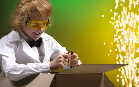 Scientific experiment. Cheerful little boy sitting a the cardboard box and testing wires while isolated on coloured の写真素材