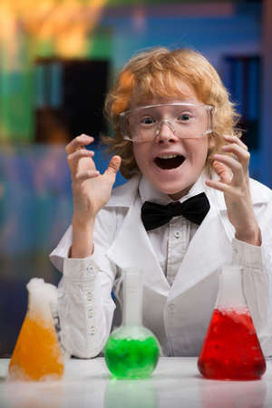 I did it! Happy little boy in lab coat gesturing while sitting at the table with laboratory equipment on itの写真素材