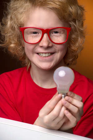 Boy with a light bulb. Cheerful red hair boy in glasses holding a light bulb and smiling at camera