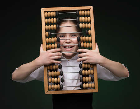 Girl with abacus. Happy little girl looking through abacus and smiling while standing isolated on blackの写真素材