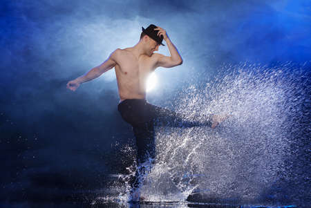 Man dancing in water. Young male dancer in black fedora dancing on the wet floorの写真素材