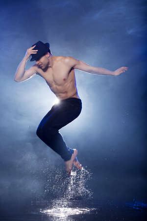 Jumping in aqua studio. Young male dancer in black fedora dancing on the wet floorの写真素材
