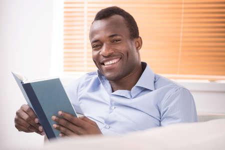 Reading an exciting book. Cheerful African descent reading a book and smiling at cameraの写真素材