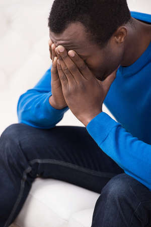 Depressed men. Top view of sad African descent men sitting on the couch and covering his face with handsの写真素材