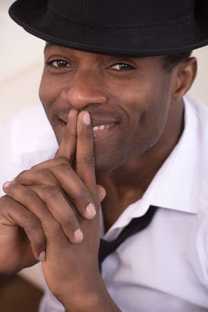 Creative soul. Cheerful African descent men in fedora holding his fingers as a gun near face and...