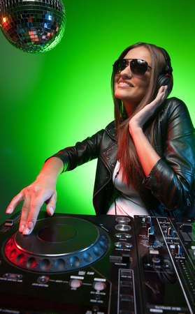 Female DJ at work. Beautiful young female DJ in headphones spinning on  turntableの写真素材