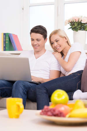 Using computer together. Beautiful young couple sitting close to each other and looking at the laptopの写真素材