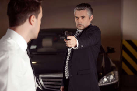 Dirty business. Confident mature men in formalwear aiming another men with gunの写真素材