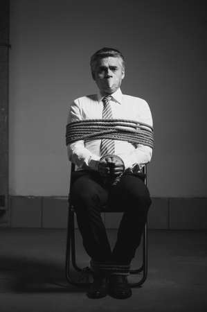 Kidnapped businessman. Black and white image of tied up businessman sitting at the chair and looking...
