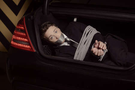 Kidnapped businessman. Tied up young men lying in the car trunk and looking at camera