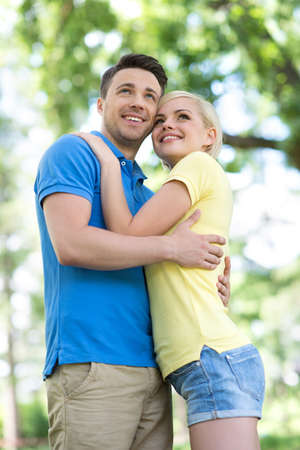 Low angle view of young loving couple hugging and looking awayの写真素材
