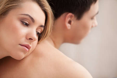 Relationship difficulties. Young depressed woman leaning at her boyfriend back and looking awayの写真素材